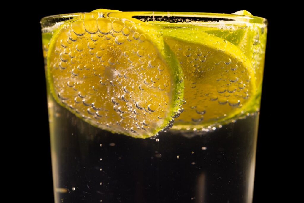 A glass of clear light yellow red onion tonic with a slice of lemon on the rim ready to drink