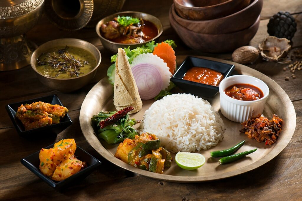 A colourful array of small bowls containing various Indian fermented foods such as curd with fruit chaas in a glass idli