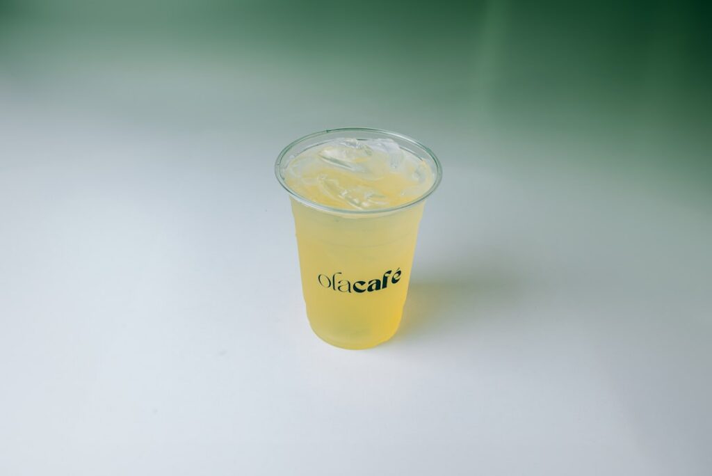 A glass of freshly blended green aloe vera tonic with a slice of lemon next to a spoon with raw honey on a rustic wooden
