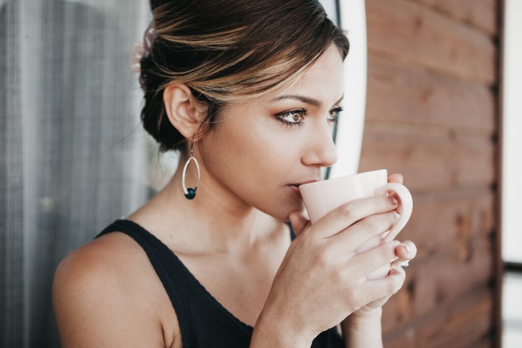 A woman holding a clear glass of a yellowish liquid representing the prepared Zesty 4-in-1 blend with a serene expressio