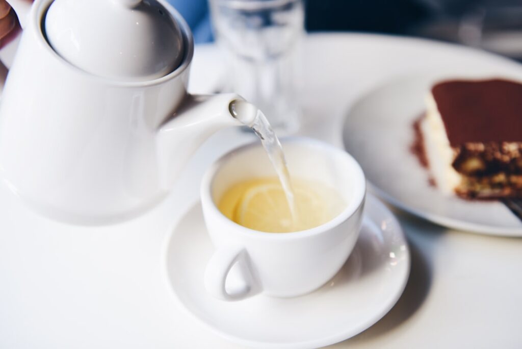 A glass teapot pouring amber-colored Mullein tea into a ceramic cup with fresh Mullein leaves and a jar of honey nearby