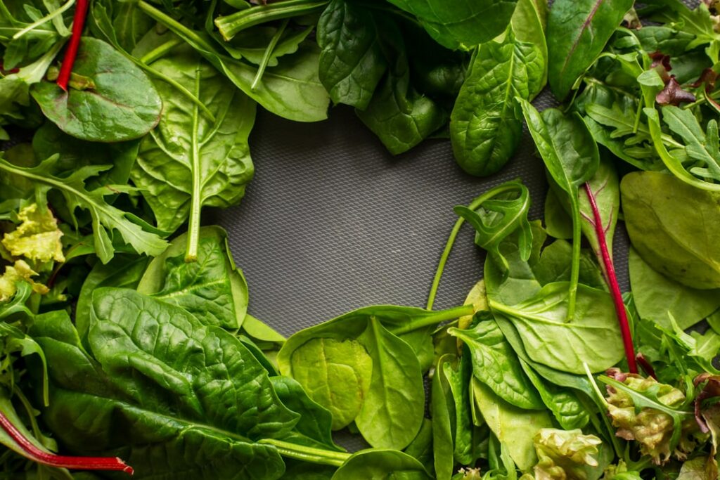 A close-up of fresh vibrant leafy green vegetables like spinach and kale with some berries scattered around