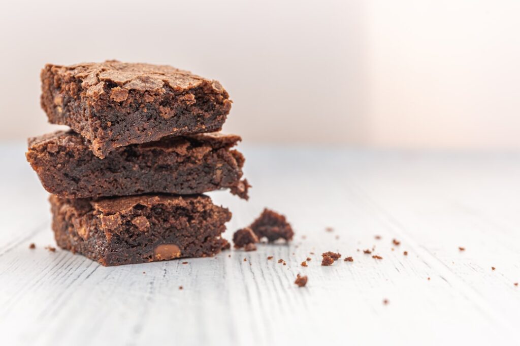 A close-up shot of perfectly fudgy vegan brownies arranged on a rustic wooden board with a sprinkle of cocoa powder or s
