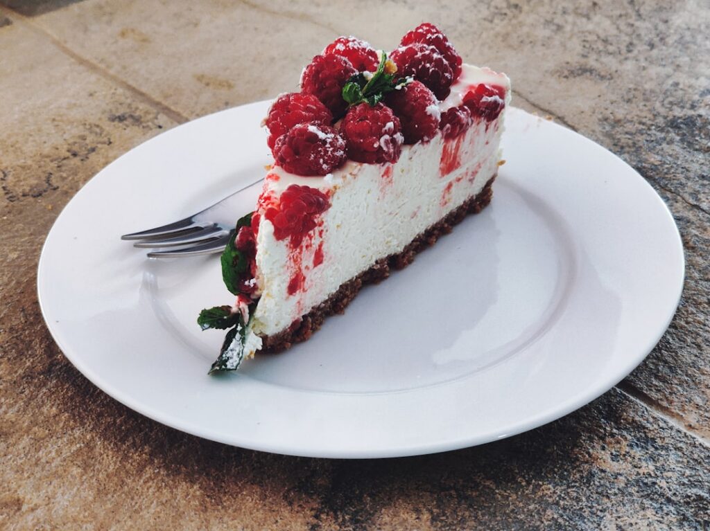 A slice of creamy no-bake vegan cheesecake topped with fresh mixed berries and a sprig of mint served on a rustic plate