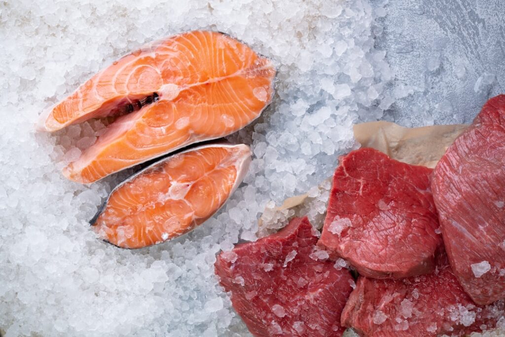 Close-up of fresh fish fillets stored on ice in a clear container inside a refrigerator