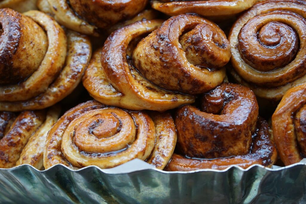 A close-up of a perfectly baked frosted cinnamon roll being pulled apart showing its soft layers and gooey filling
