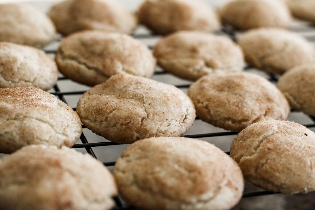 A close-up of a stack of freshly baked snickerdoodle cookies coated in cinnamon sugar next to a small bowl of cinnamon s