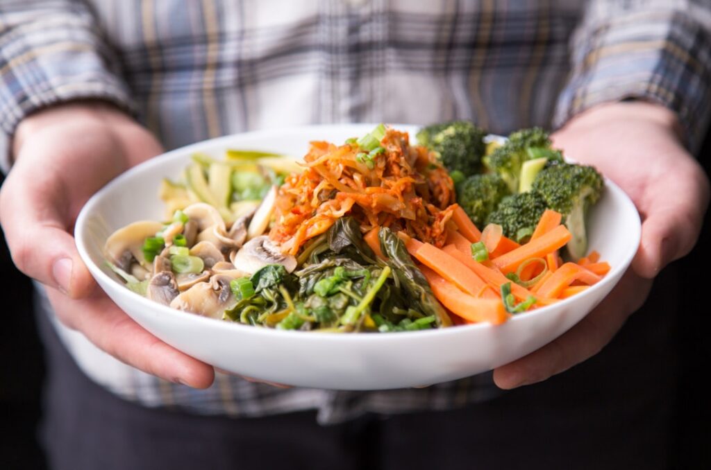 A beautifully arranged bowl of vegan ramen with colorful vegetables tofu and noodles in a rich broth garnished with fres