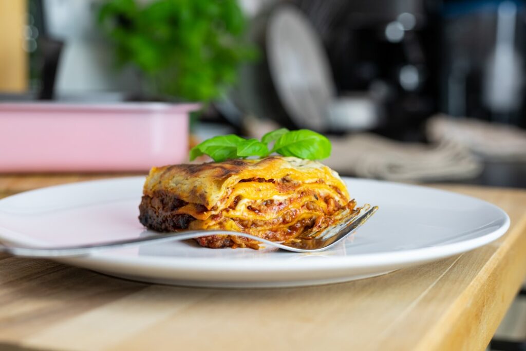 A beautifully plated slice of vegan lasagna showing visible layers of pasta rich red sauce green vegetables and creamy w