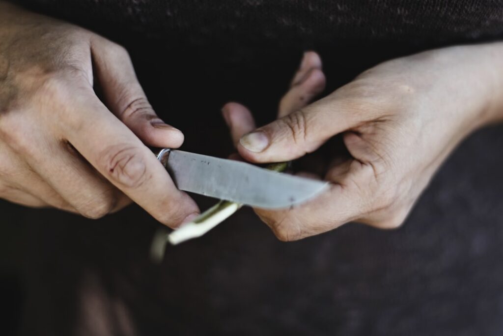 Close-up of human hands carefully collecting milky white sap from a green wild lettuce stem into a small glass vial