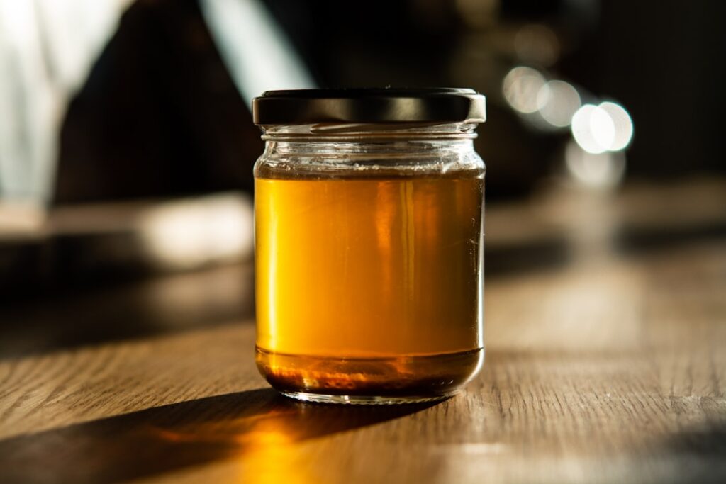 Gnarled wild lettuce roots submerged in a liquid inside a glass jar on a wooden table suggesting a tincture or infusion 