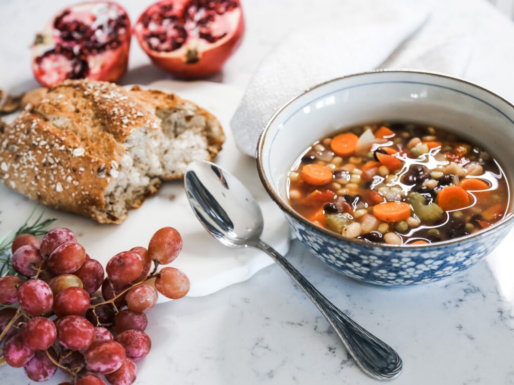 A steaming bowl of chickpea noodle soup garnished with fresh herbs in a cozy setting with a wooden spoon