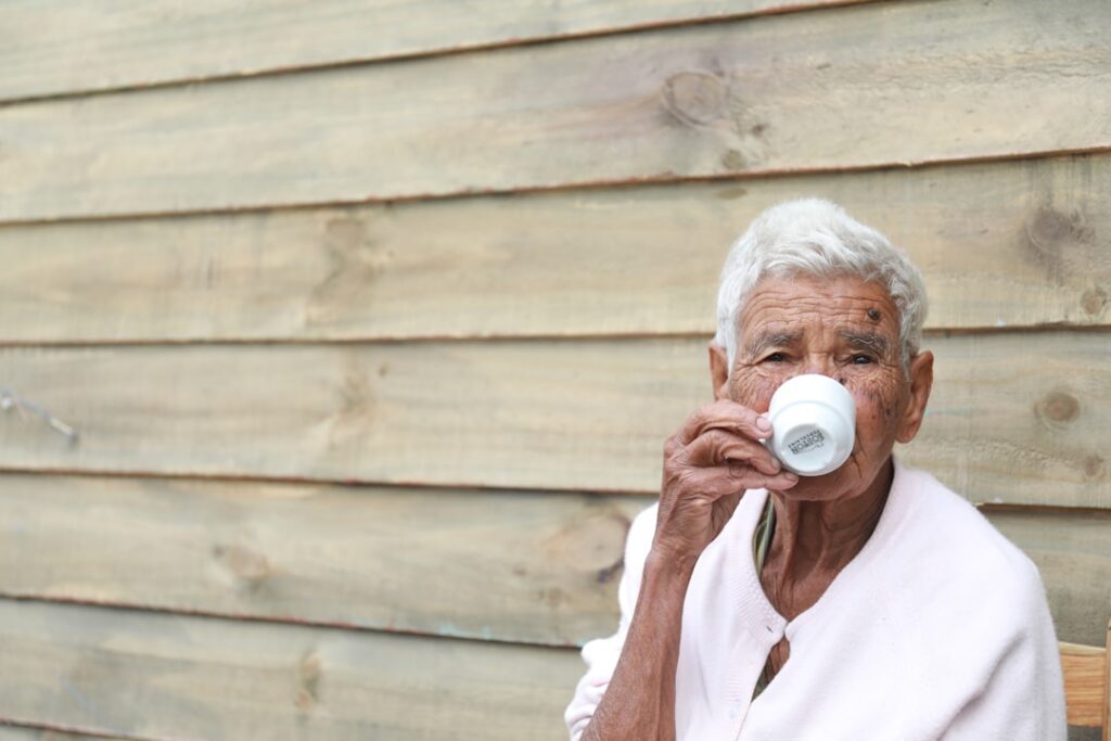 An elderly person perhaps a woman with a warm steaming mug in their hands looking content and healthy possibly in a cozy