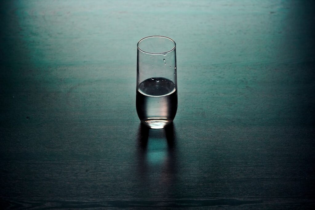 Four transparent glasses all filled to the same water level Each glass contains a different object scissors a paper clip
