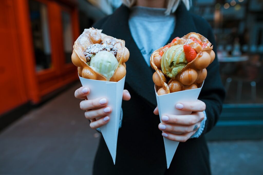 A close-up of hands gently shaping a hot freshly cooked waffle into a cone using a wooden cone roller