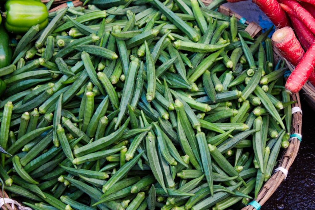 Close-up of fresh green okra pods on a rustic wooden surface perhaps with a few sliced open to show the mucilage