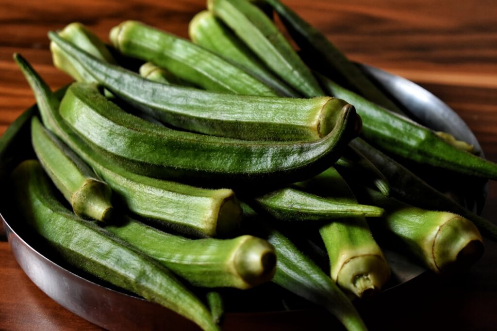 A collection of ingredients for the DIY okra gel fresh okra a bottle of aloe vera gel and a small container of vitamin E