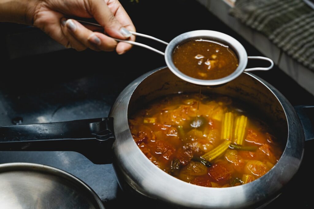 A person s hands straining blended okra through a fine-mesh sieve into a glass bowl to create a smooth gel