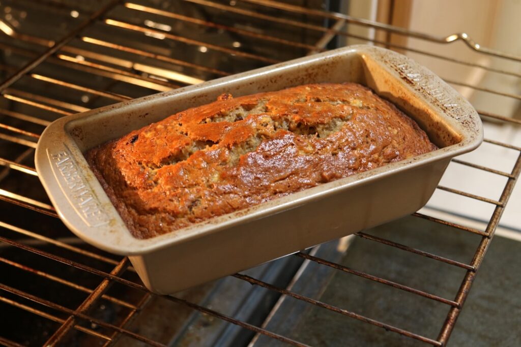 A perfectly baked vegan banana bread loaf on a cooling rack with steam gently rising highlighting its golden-brown crust