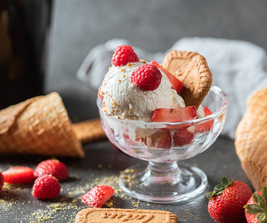 A perfectly scooped bowl of homemade vanilla ice cream garnished with a vanilla bean and a fresh berry showcasing its cr