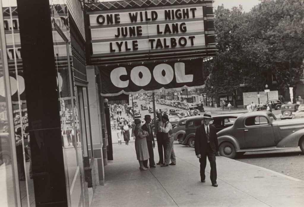 A retro movie theater marquee from the 1980s showing a classic movie title with people lining up for tickets