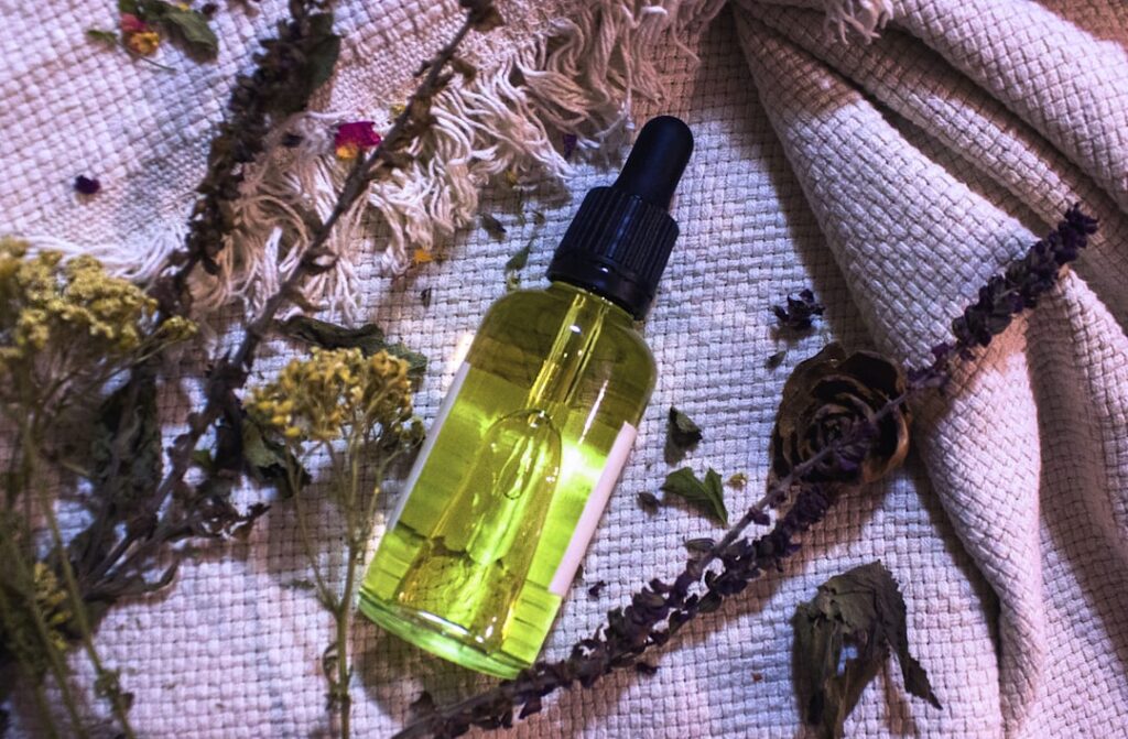 A beautiful glass bottle of golden infused oil with visible natural botanicals like rose petals or calendula flowers ins