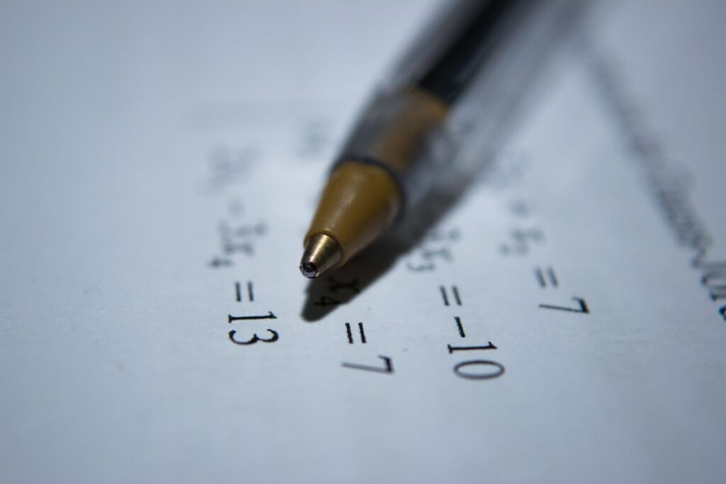 A person s hand holding a pen poised over a notepad with mathematical equations or a puzzle written on it A cup of coffe