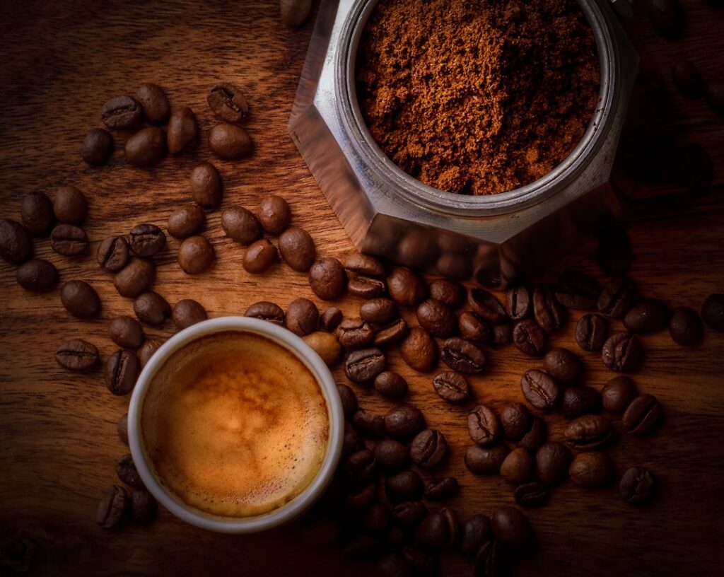 A close-up shot of a small bowl containing a mixture of coffee grounds and Vaseline with a spoon or spatula beside it hi