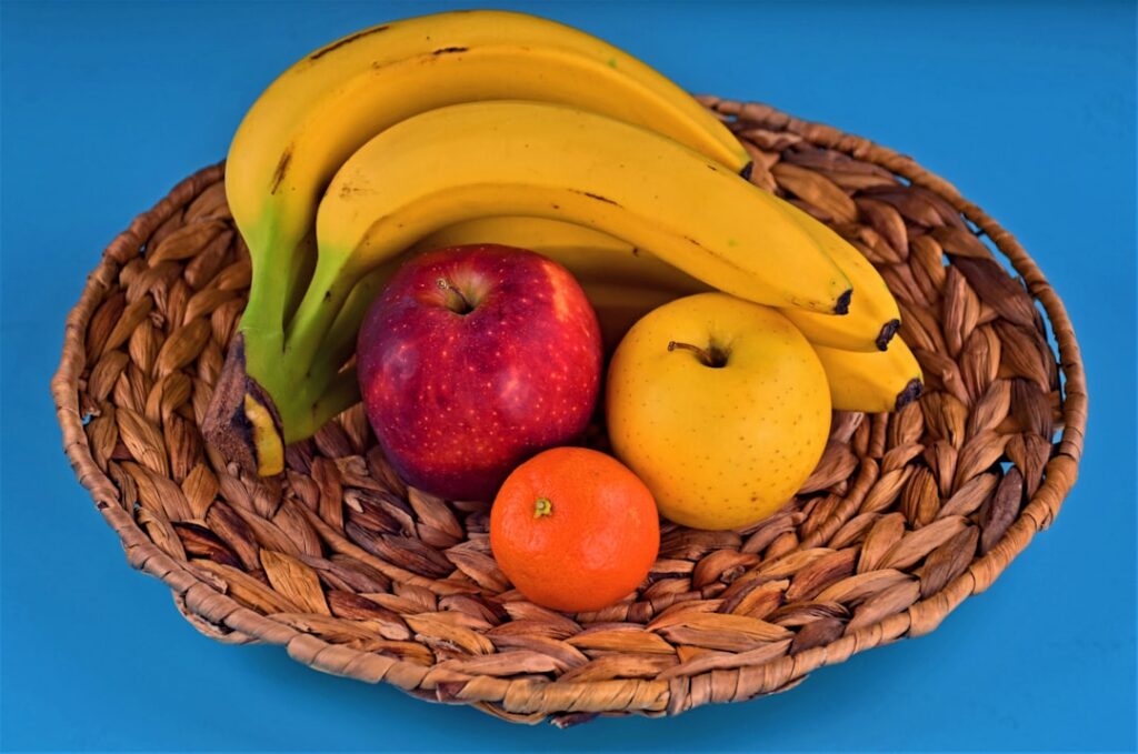 A colorful visual math puzzle featuring three equations with illustrations of red apples and bunches of yellow bananas f