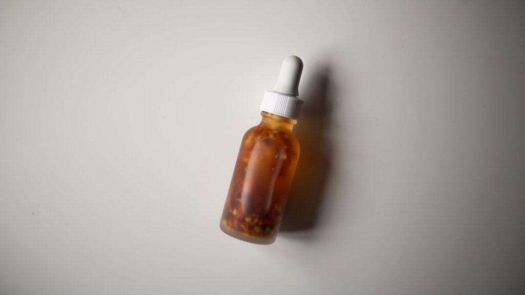 A clear glass dropper bottle filled with a golden-yellow oil serum surrounded by a small bowl of turmeric powder whole c