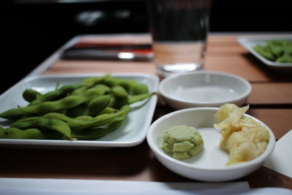 A vibrant bowl of steamed edamame pods sprinkled with sea salt next to a small dish of shelled roasted edamame for snack