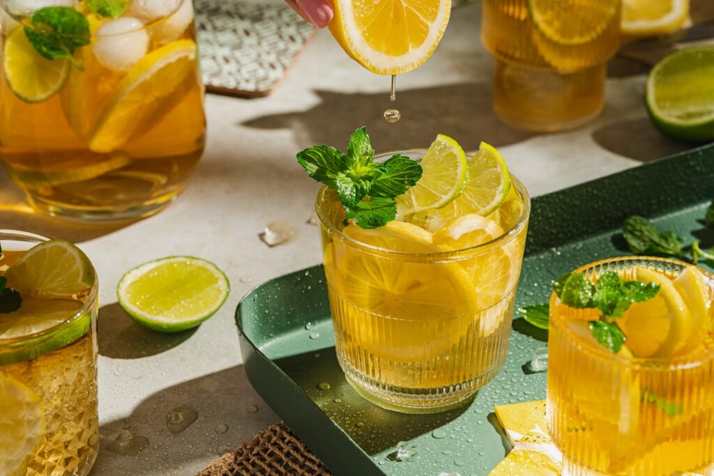 A vibrant yellow drink in a clear glass garnished with a lemon slice and a sprinkle of turmeric Ingredients like collage