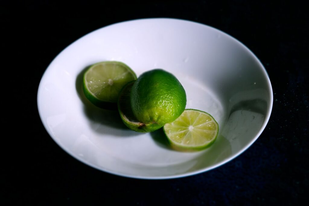 A close-up of a small bowl containing a white cornstarch and lime juice mixture with a fresh green lime half and a spoon