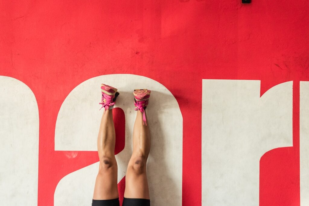 A woman demonstrating the Wall Press exercise showing proper form with hands shoulder-width apart on a wall and body in 