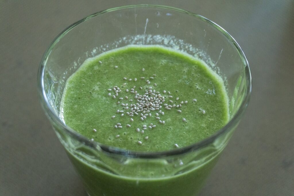 A vibrant healthy green breakfast smoothie in a tall glass garnished with fresh spinach banana slices and chia seeds sit
