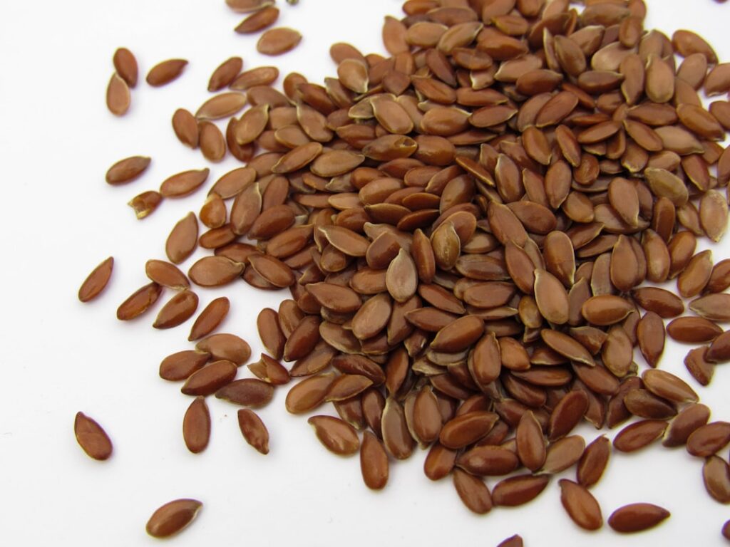 Close-up of a small glass jar filled with clear thick flaxseed gel with some whole flaxseeds visible in the background o