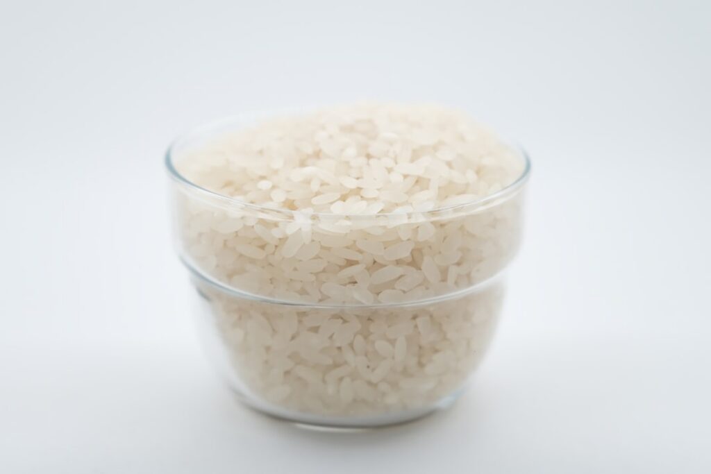 White rice grains in a wooden bowl with a clear glass jar containing a thick white rice gel A few rice grains are scatte