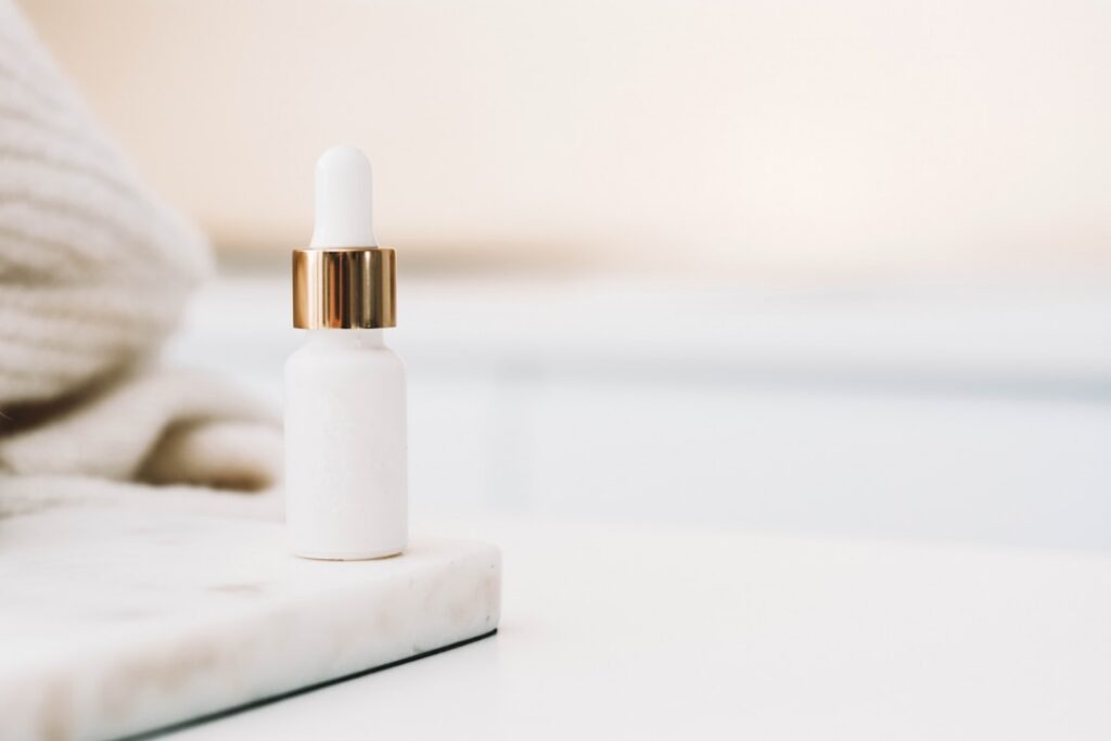 A close-up shot of a small clear bottle of baby oil on a soft light-colored fabric with a few drops of oil glistening on