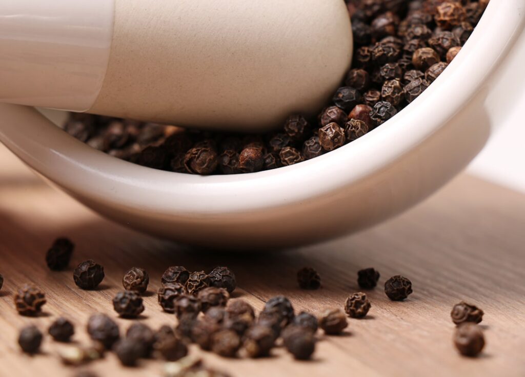 Close up of a mortar and pestle grinding black peppercorns into a fine powder
