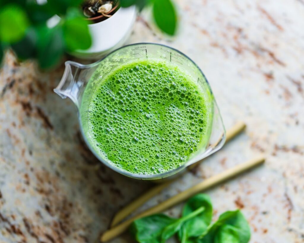 A vibrant fresh green smoothie or juice in a clear glass with fresh greens and fruits like spinach kale apple and ginger