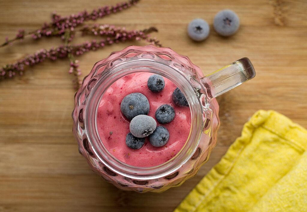 A perfectly smooth and creamy purple blueberry smoothie being poured from a blender into a tall glass garnished with fre