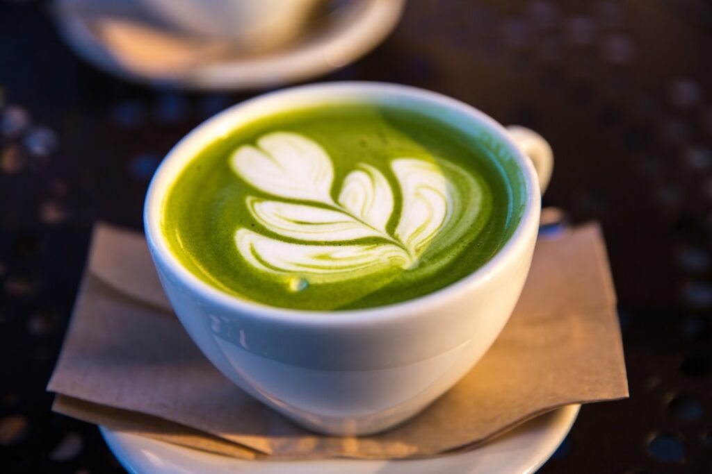 A Pinterest-friendly image of a creamy vibrant green matcha latte in a ceramic mug with a sprinkle of matcha powder on t