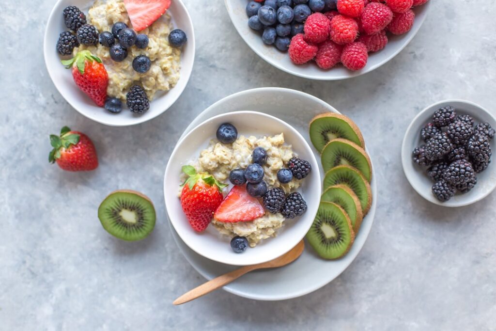 Three separate bowls of cooked oatmeal one with steel cut oats topped with blueberries and almonds one with old fashione