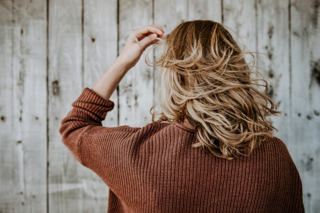 A person gently massaging a natural hair oil into their scalp with healthy shiny hair
