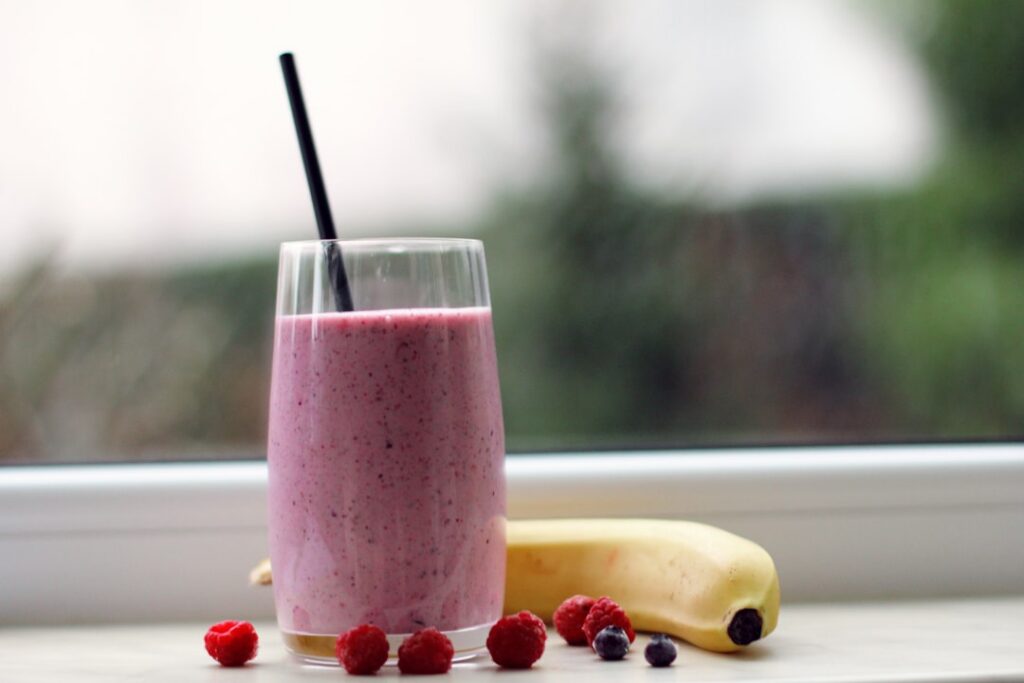 A refreshing and vibrant banana smoothie in a glass with a straw garnished with a slice of banana or a mint leaf