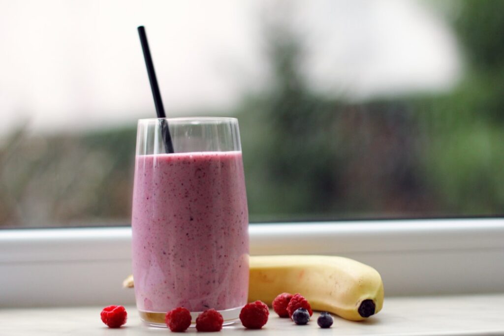 A vibrant purple berry smoothie topped with fresh berries and a sprinkle of ground flaxseed next to a bowl of ground fla