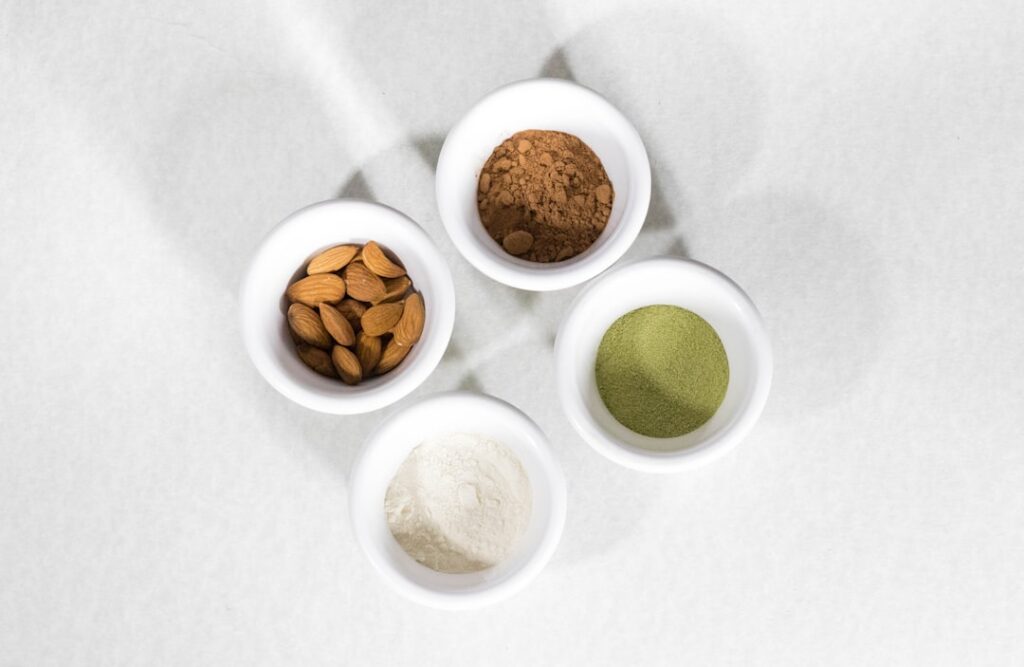 A plate of neatly arranged matcha protein balls dusted with matcha powder alongside some raw ingredients like dates and 