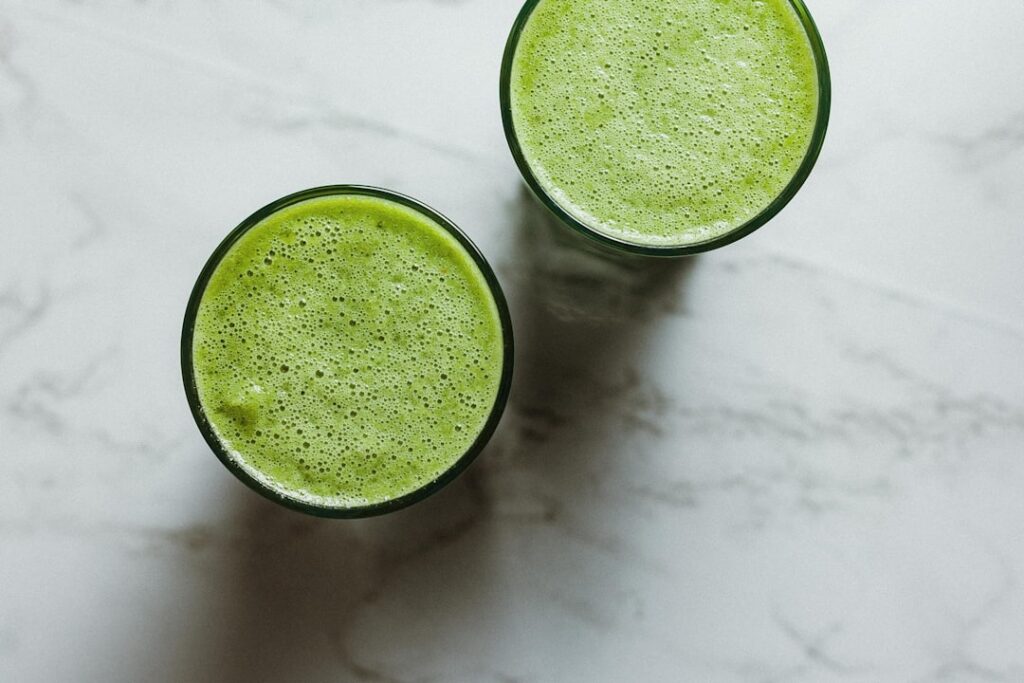 A bright green smoothie in a glass garnished with fresh mint and a slice of lime surrounded by fresh spinach green apple