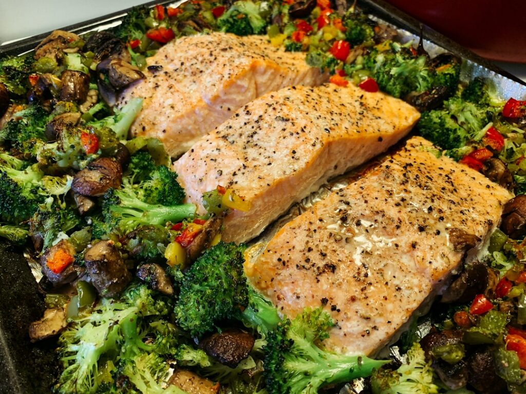 A balanced and colorful dinner plate featuring a baked salmon fillet alongside roasted broccoli florets and sweet potato