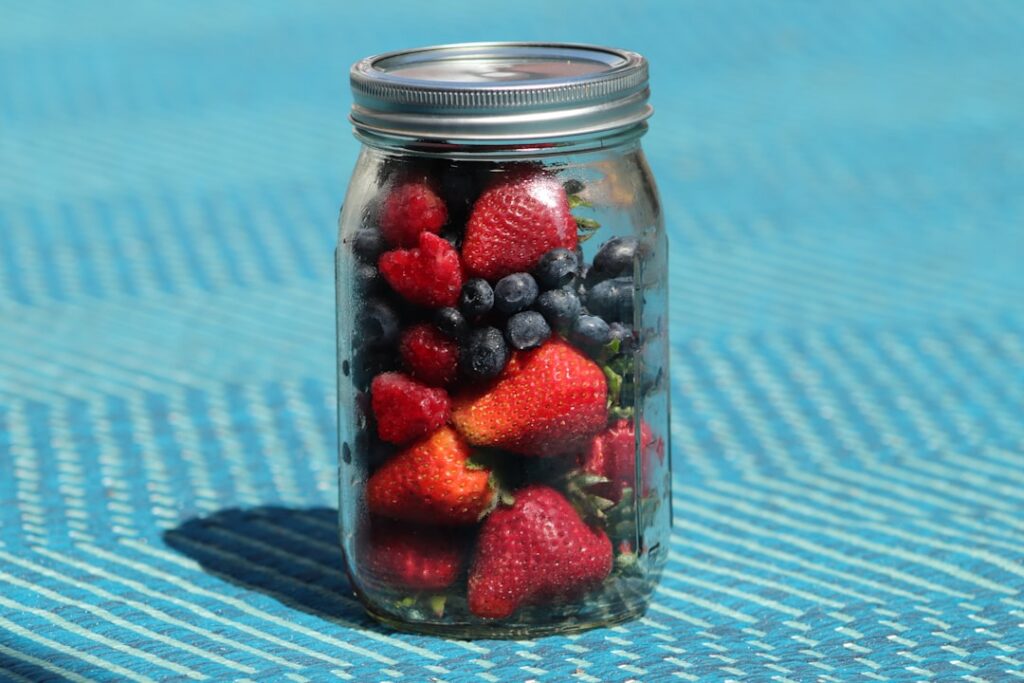 A glass jar of prepared overnight oats with layers of chia pudding strawberries rolled oats blueberries and walnuts with